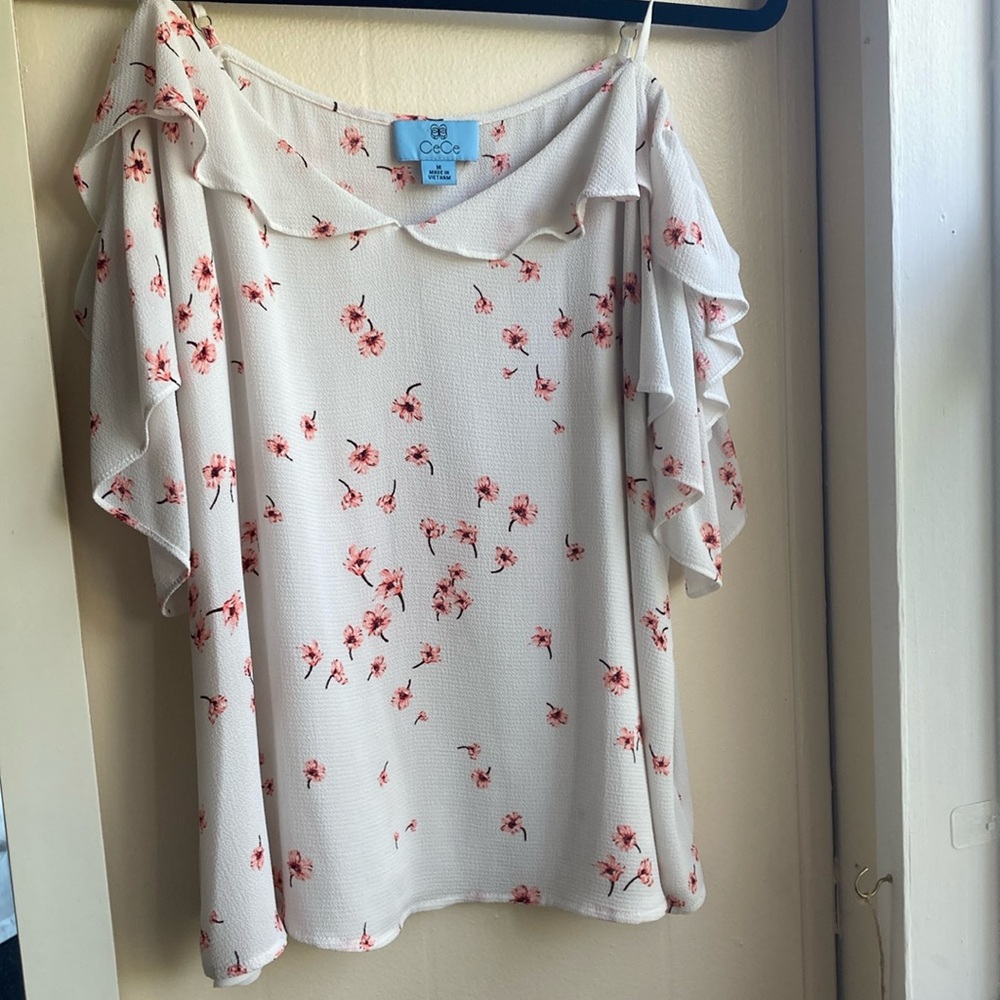 White blouse with pink flowers. It has sleeves that go down on the shoulders